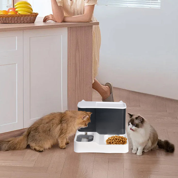 A sleek white and gray 2-in-1 pet feeder and water dispenser sits on a wooden floor, with two cats nearby.